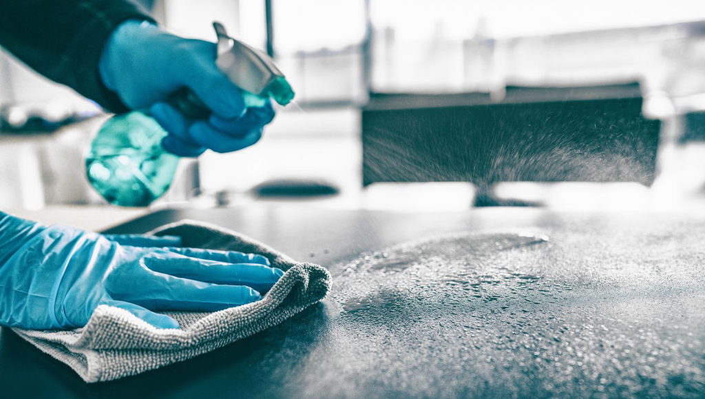 Person cleaning a surface with spray cleaner and a cloth, wearing blue gloves. Cleaning, disinfecting, and hygiene concept.