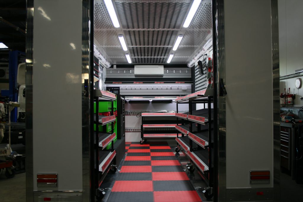 Inside view of a customized white work truck or trailer, featuring shelving and a black and red checkerboard floor.