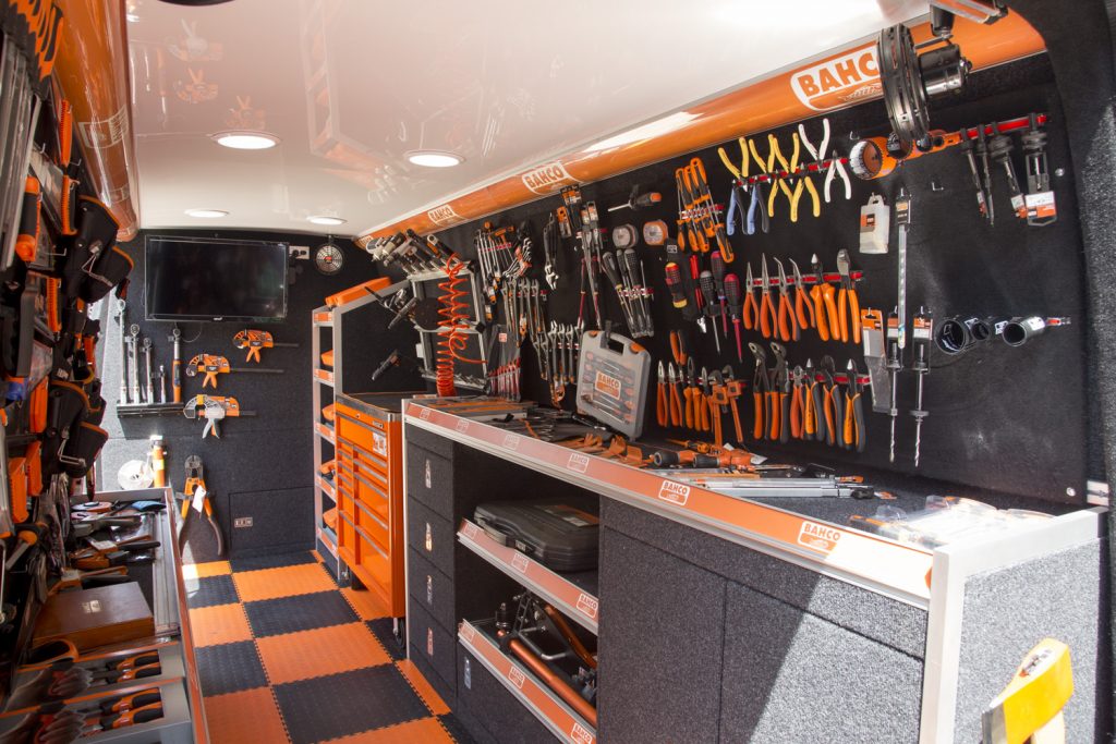 Mobile workshop interior with tool storage, work surfaces, and a variety of hand tools organized on the walls, showcasing a practical design.