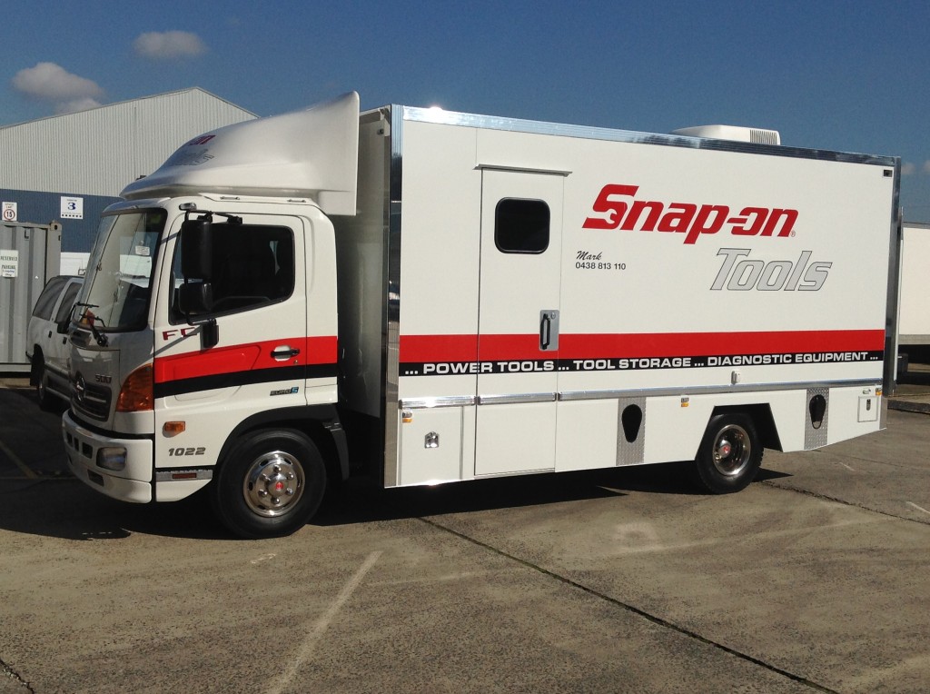 White Snap-on Tools delivery truck parked on concrete under a blue sky, featuring the company logo and contact information on the side.