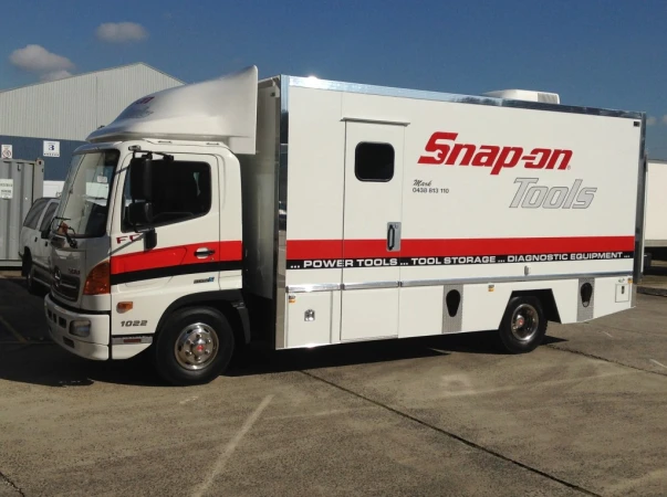 White Snap-on Tools delivery truck parked on concrete under a blue sky, featuring the company logo and contact information on the side.