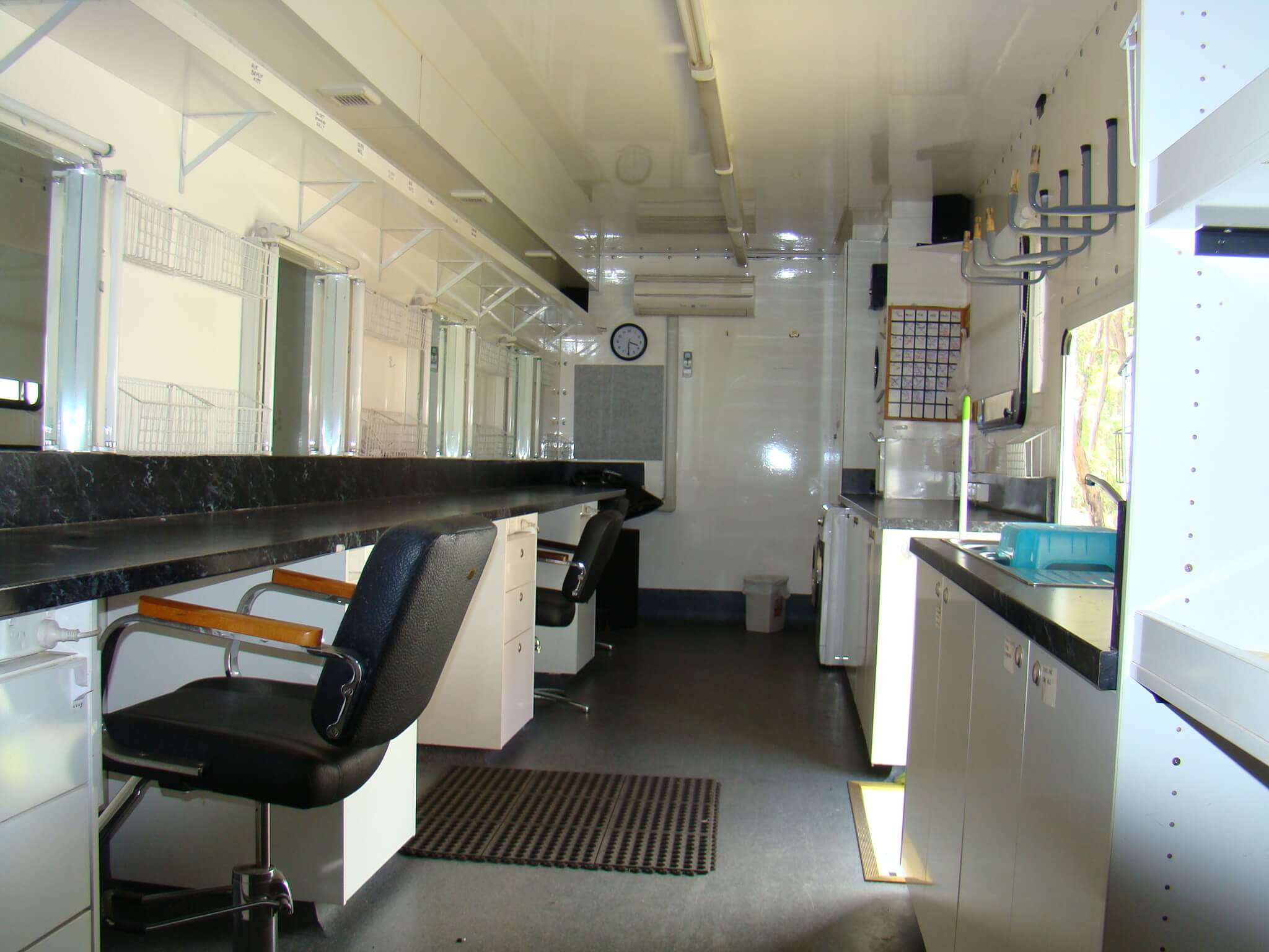 Interior view of a mobile salon featuring styling chairs, mirrors, counters, and cabinets, all within a trailer-like setting.