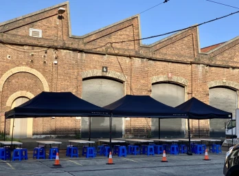 Three black pop-up canopies set up in front of a historic industrial brick building with large arched doors in Sydney.