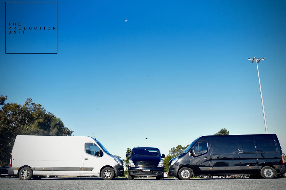 Three production vans parked in a row under a clear blue sky in Sydney, with a white van on the left and two black vans.