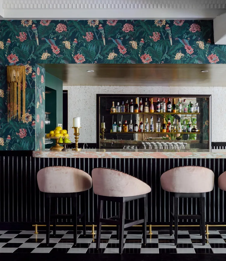 Interior shot of a bar featuring pale pink barstools, a black and white checkered floor, and floral wallpaper in a restaurant.