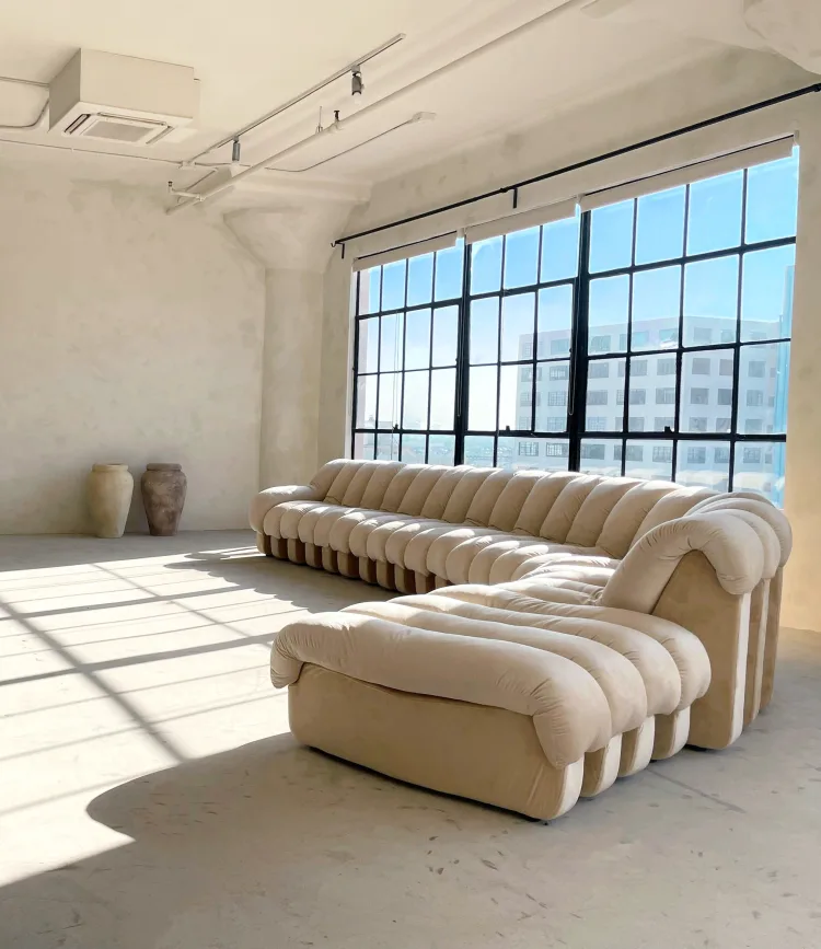 Interior photography of a sectional sofa in a bright, minimalist photo studio with concrete floors and large industrial windows.