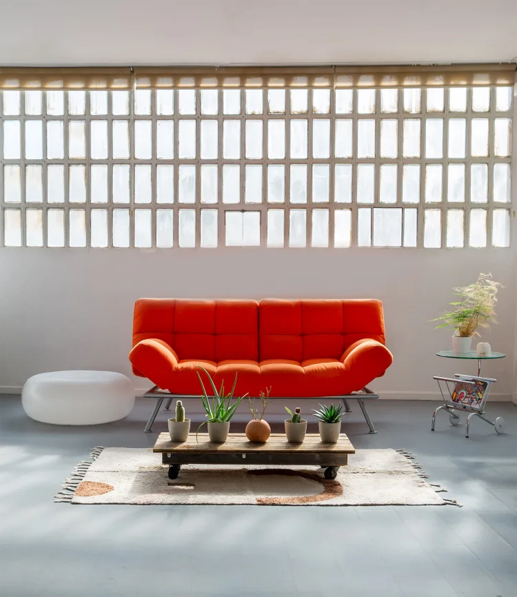 Stylish living room interior featuring an orange sofa, plants, a wooden coffee table, and natural light from a large window.