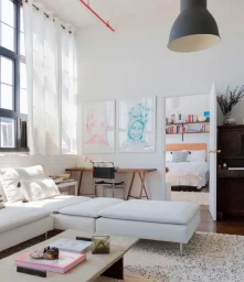 Bright modern living room interior with a white sectional sofa, large windows with white curtains, and artwork on the wall.
