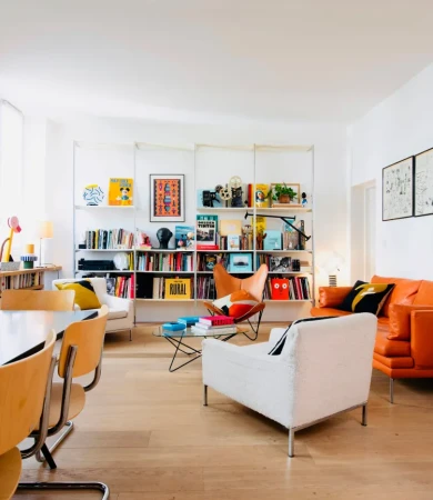 Modern living room interior with orange leather sofa, white armchairs, and a large white shelving unit filled with books