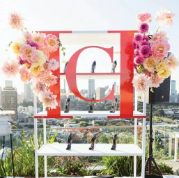 White display shelf with a large red letter C, high heels, and floral arrangements on a Sydney rooftop overlooking the city skyline.