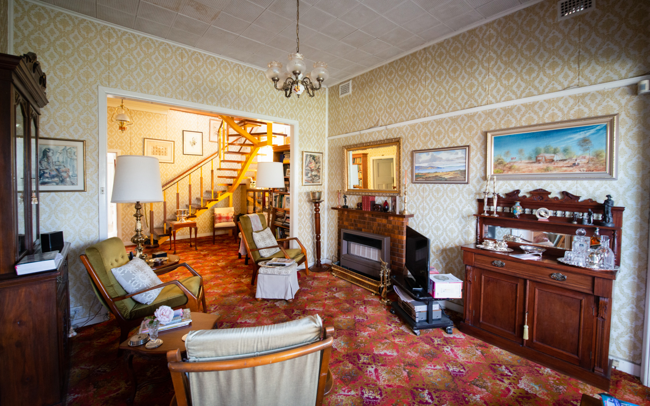 Interior living room view with patterned wallpaper, armchairs, decorative furniture, and stairs leading to an upper level.