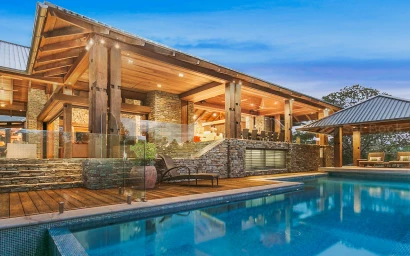 Modern luxury house exterior with a swimming pool, wooden beams, stone pillars, and outdoor decking in Sydney.