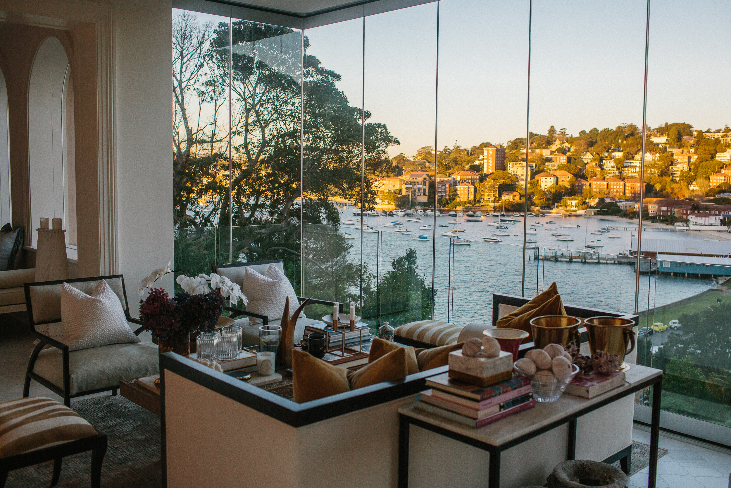 Sunlit living room with bay window offers views of the waterfront, showcasing interior design elements, luxury furniture, and decorative objects.