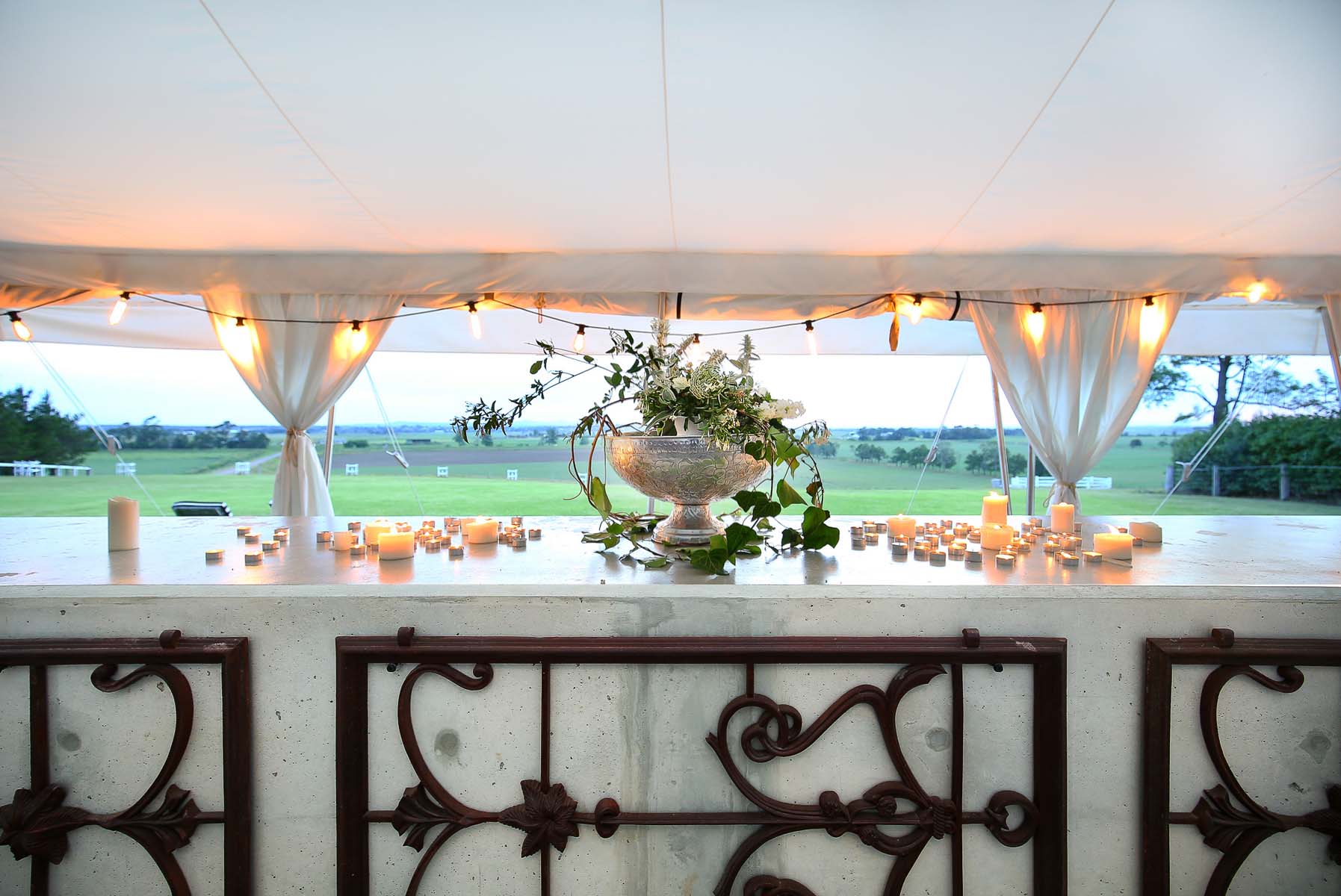 Elegant floral centerpiece and candlelight display under a tent create a warm ambiance, with an expansive outdoor backdrop.