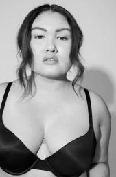 Portrait of a plus size woman wearing a black bra against a plain white studio background