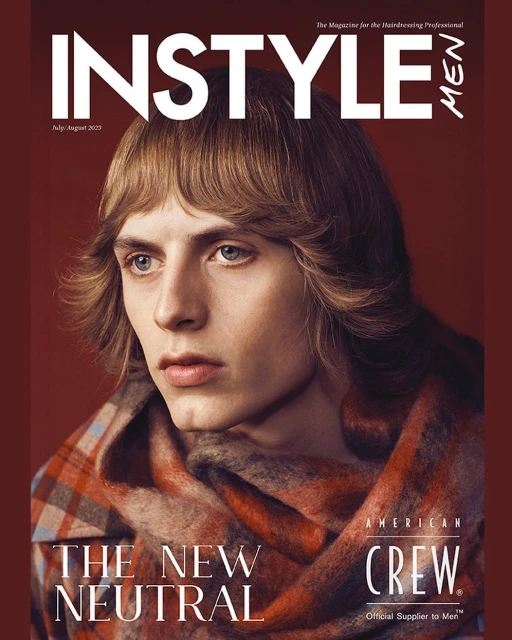 Magazine cover featuring a young adult man with long blonde hair, wearing a plaid scarf, against a reddish-brown background.