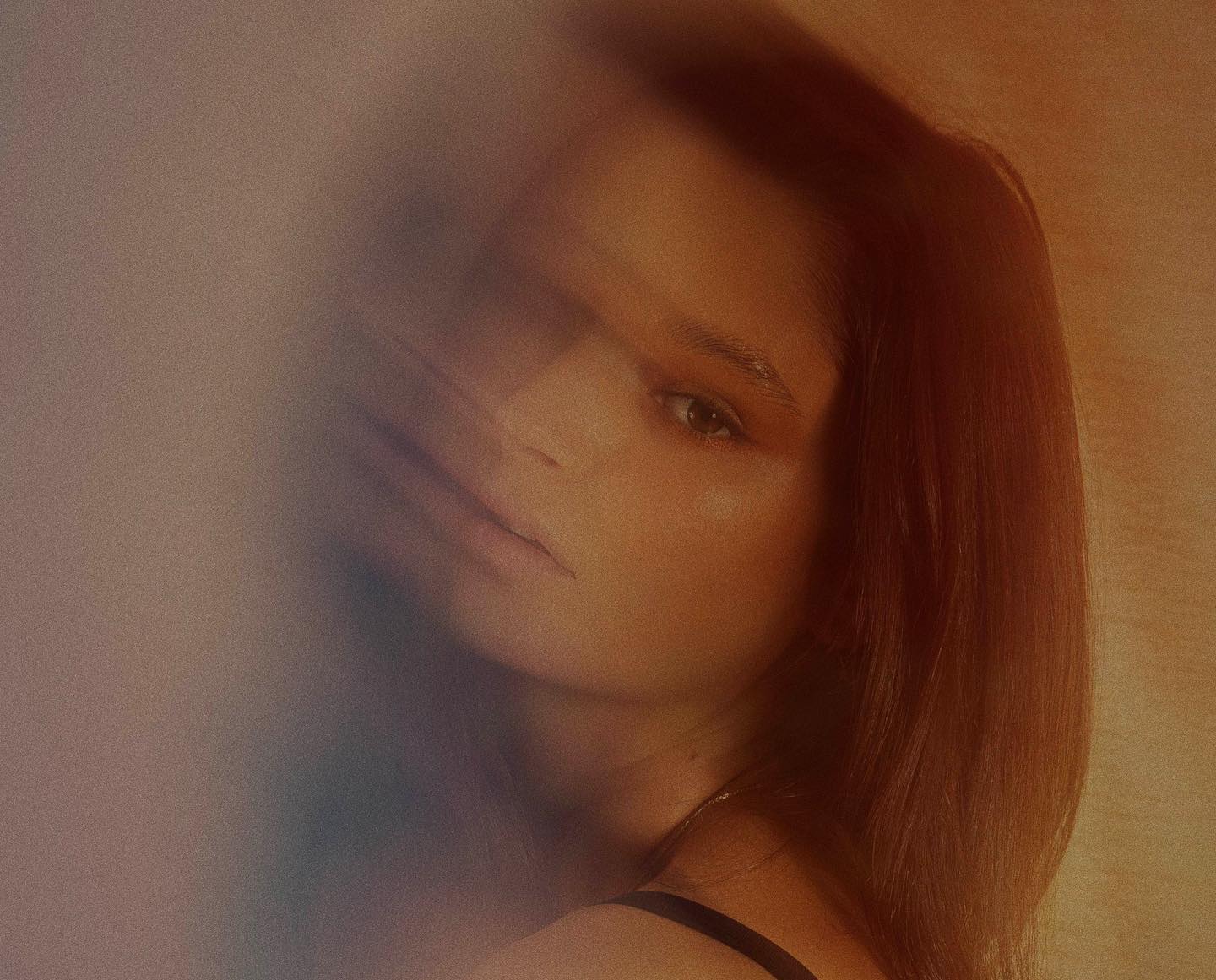 Close-up studio portrait of a young adult female with long brown hair. The soft, warm lighting creates a dreamy and sensual atmosphere.