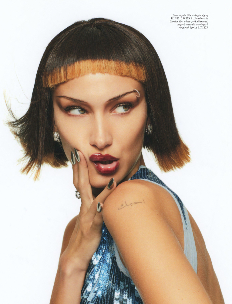 Close-up portrait of a young woman with a distinctive two-tone blunt bob haircut, wearing a blue sequined top against a white backdrop.