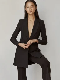 Asian female model wearing a tailored black blazer and trousers against a pale grey studio background.