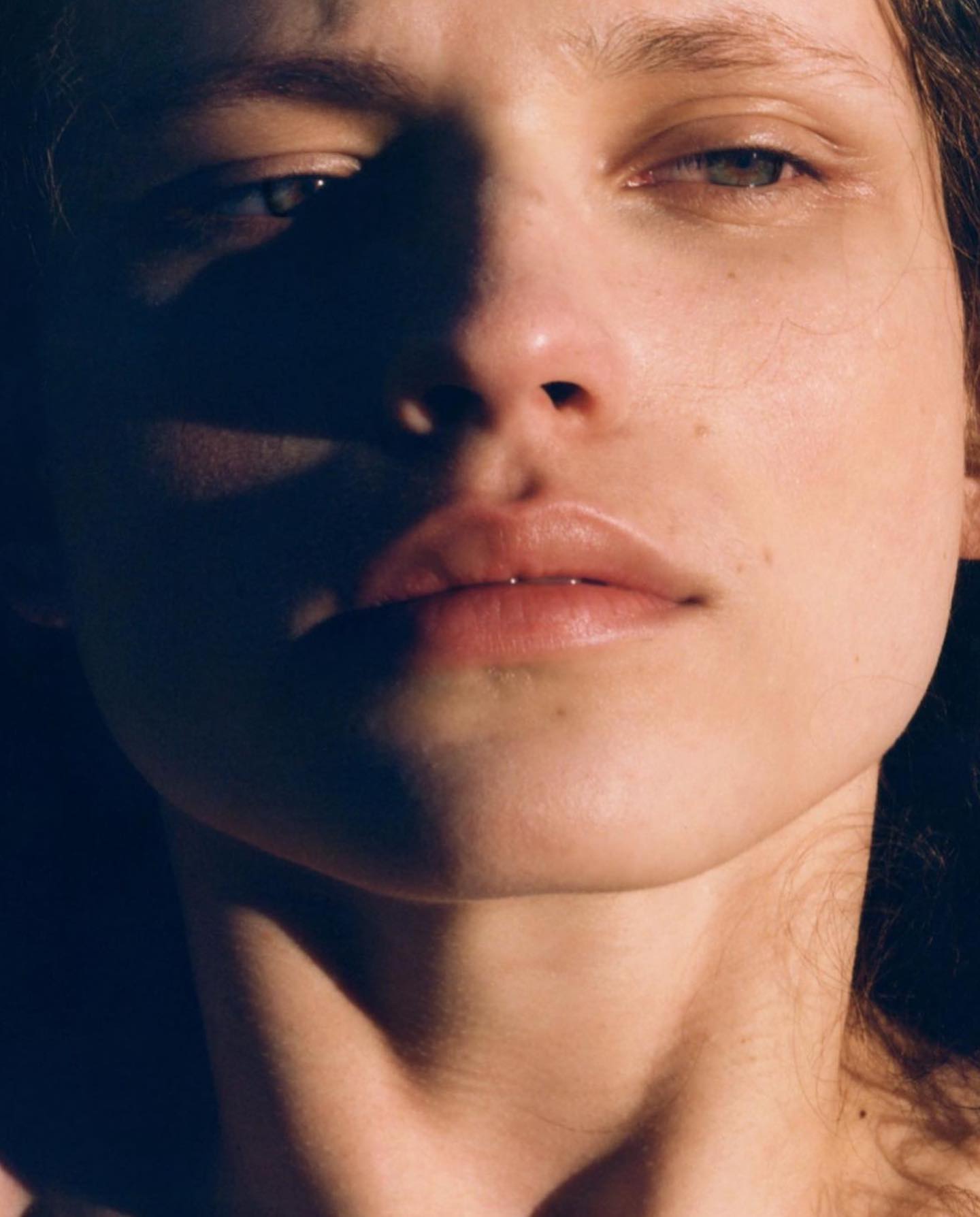 Close-up portrait of a young adult female with fair skin and light eyes, captured in dramatic lighting highlighting her facial features.