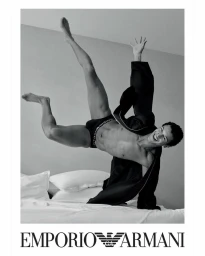 A smiling male model in underwear falling backward onto a bed in black and white.
