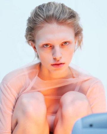 Close-up portrait of a model with blonde hair wearing a sheer peach top against a clean white background