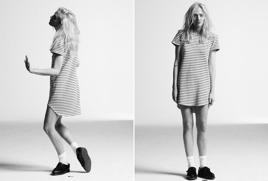Monochrome fashion shot of a woman in a striped t-shirt dress, posing in a bright studio with modern, minimalist style and cool tones.
