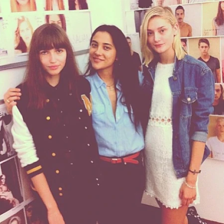 Three women posing together in an indoor space with portrait photos on the wall behind them.