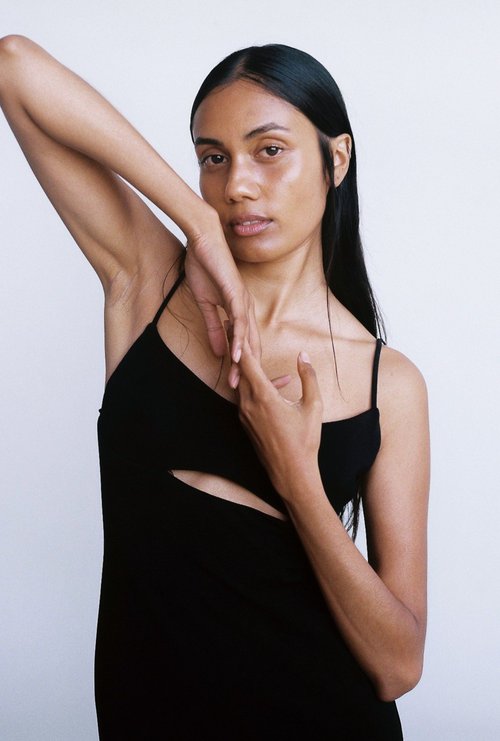 Portrait of a woman with long black hair in a black dress, posing against a white background, fashion studio photography.