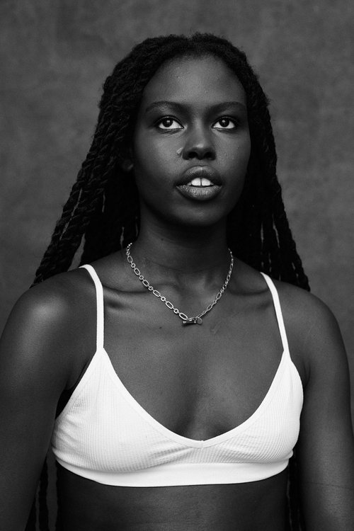 Portrait of a Black woman with long braided hair wearing a white top and a silver chain necklace.