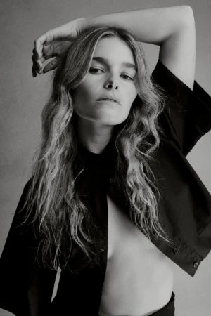Portrait of a female model with wavy hair wearing a black shirt against a plain grey background