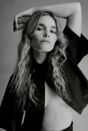 Portrait of a female model with wavy hair wearing a black shirt against a plain grey background