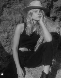 Model in wide-brim hat and dark tank top posing outdoors against a rocky terrain background