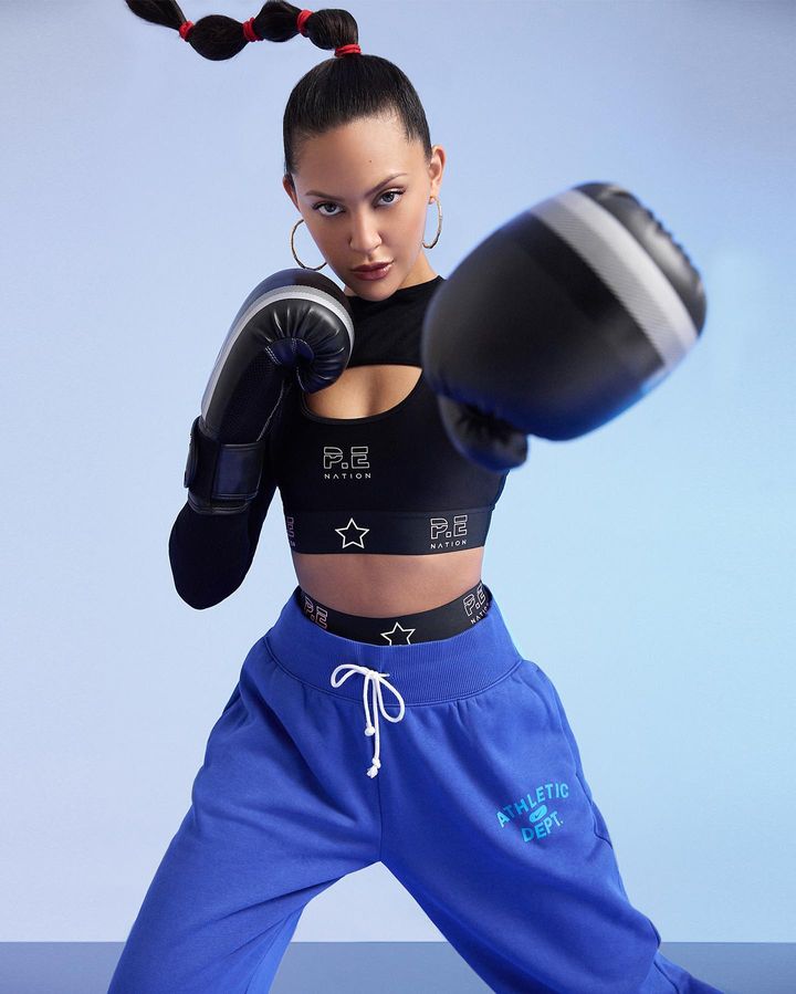 Athletic woman in boxing gloves and workout gear in a dynamic pose against a studio backdrop, showcasing fitness and determination.