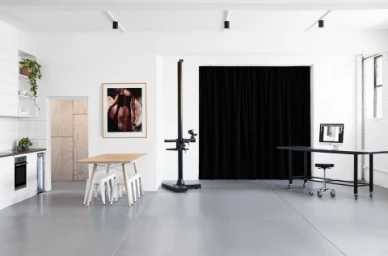 Bright, modern Melbourne photo studio interior with white brick walls, grey epoxy floors, a camera stand, and a wooden dining table.