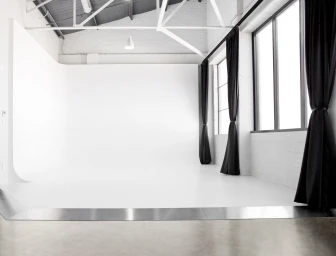 Large professional photo studio interior with a white cyclorama wall and high ceiling trusses.