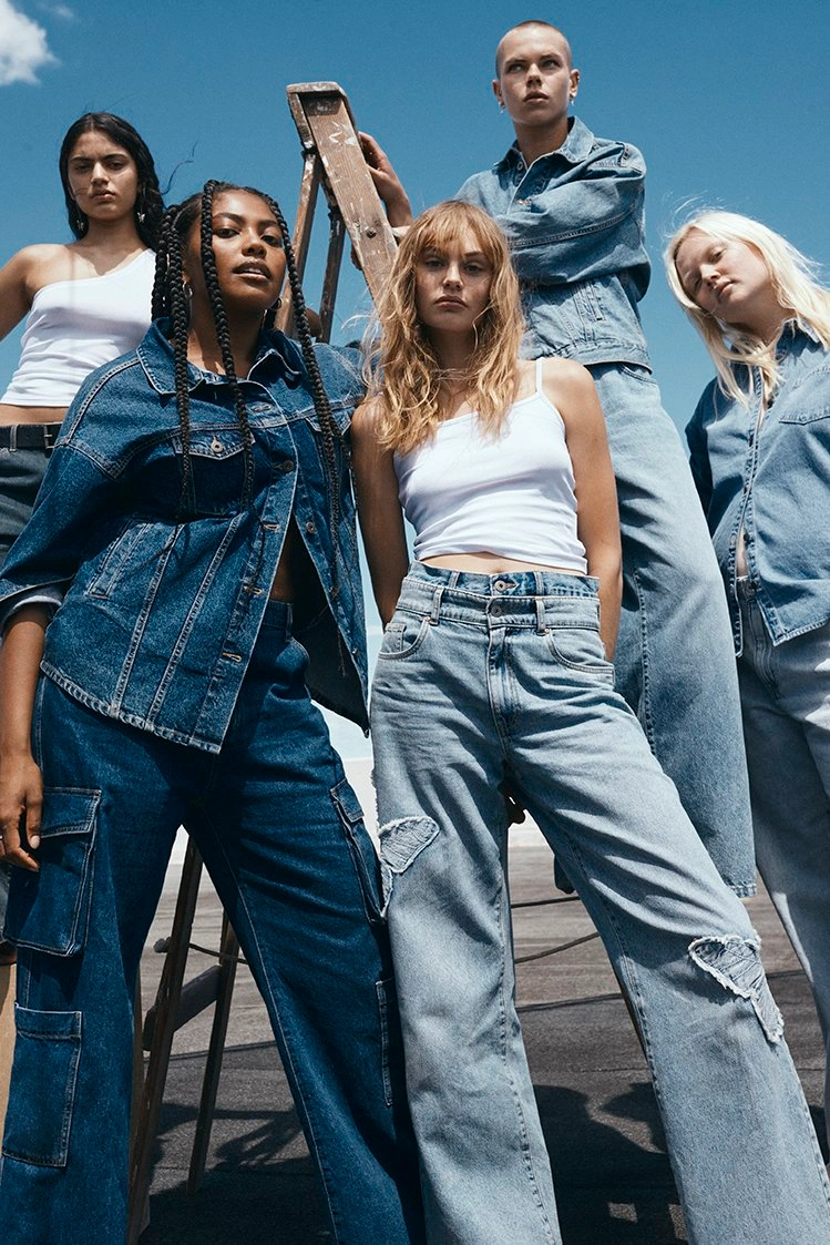Group of five diverse models wearing denim jackets and jeans posing outdoors against a clear blue sky by Chee Productions