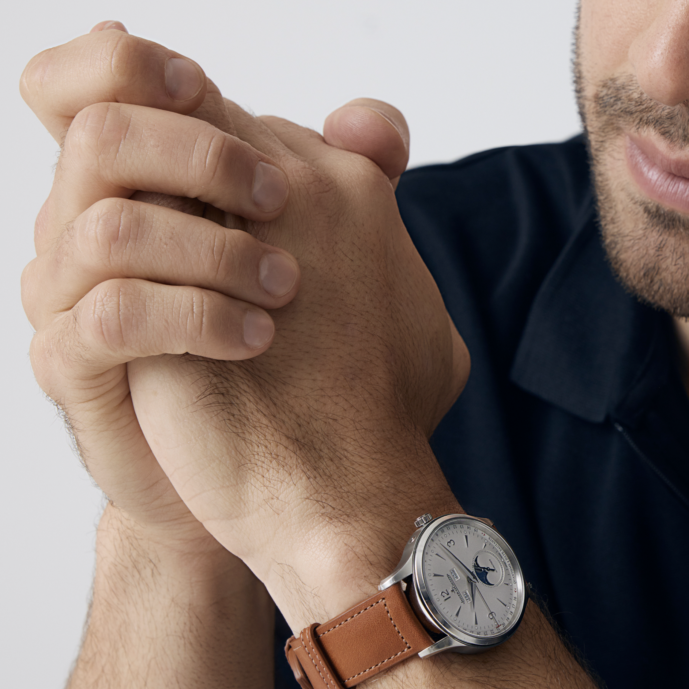 Close-up studio shot of a man's wrist with a leather-strapped watch, emphasizing the timepiece and his clasped hands in focus.