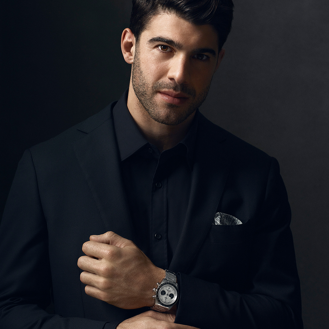 Portrait of a handsome man in a suit with a silver wristwatch, shot in a studio against a dark background, emphasizing sophistication and style.