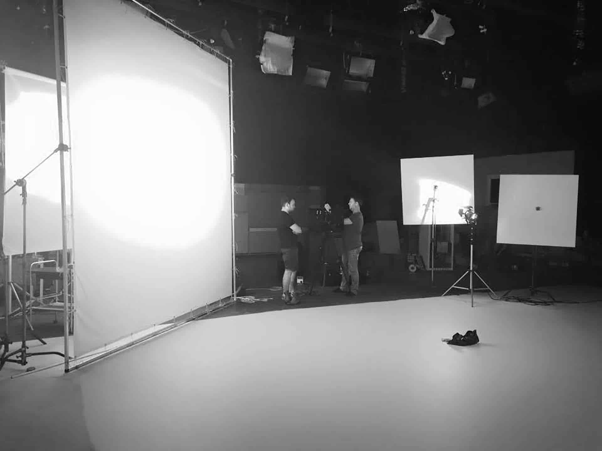 A black and white shot of a group of people working in a photo studio with lighting equipment and reflectors, standing on a bright white floor.