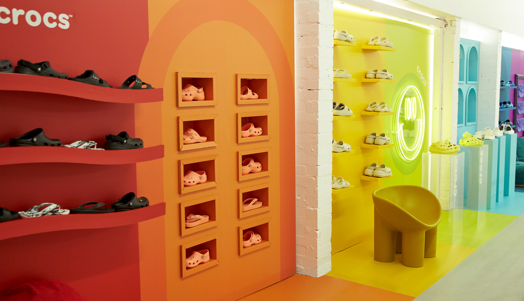 Interior of a Crocs store with shelves displaying various styles of the brand's shoes against colorful red, orange, and yellow walls.