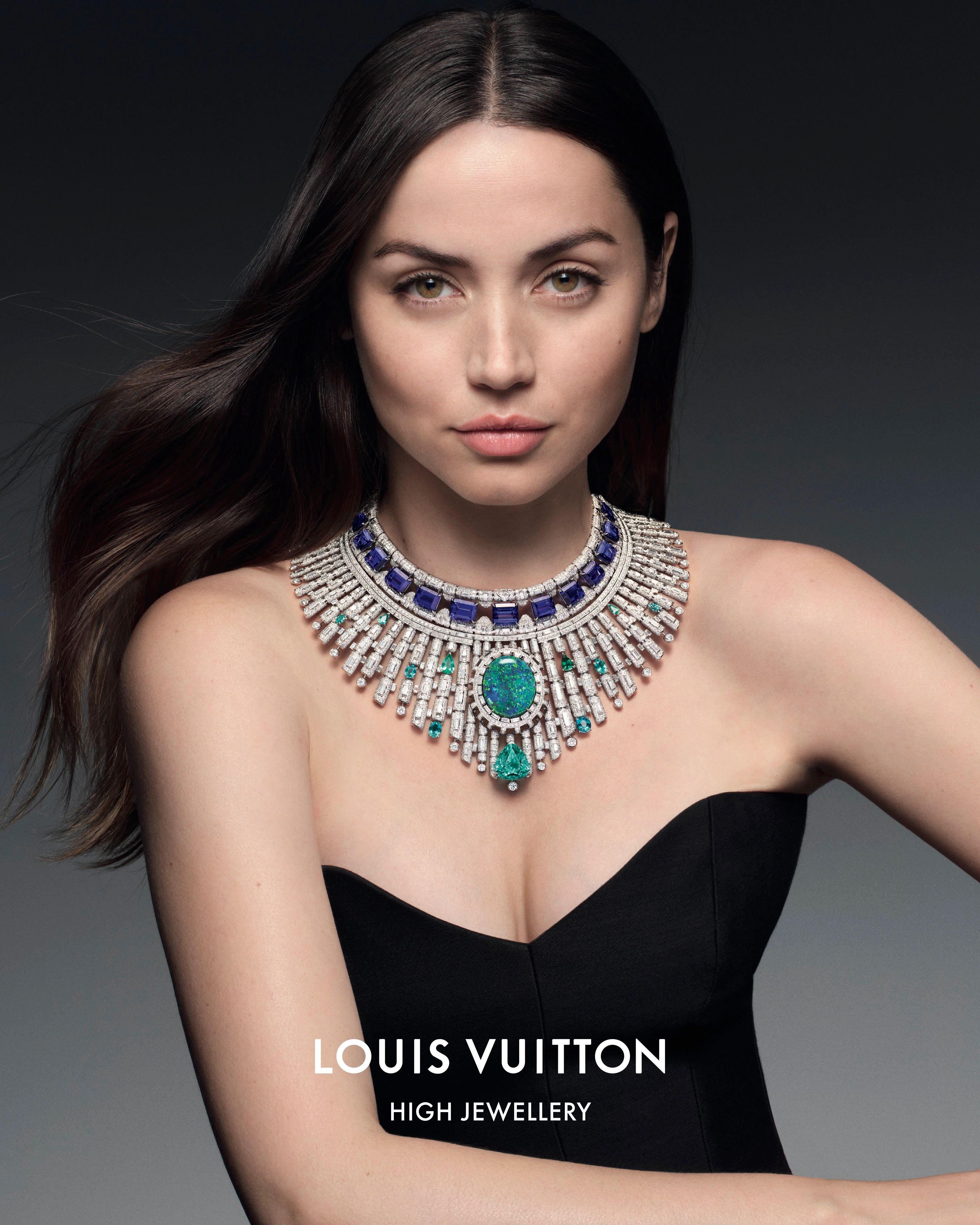 Portrait of a woman with long, dark hair wearing a black strapless dress and an ornate, multi-colored jeweled necklace by Louis Vuitton.