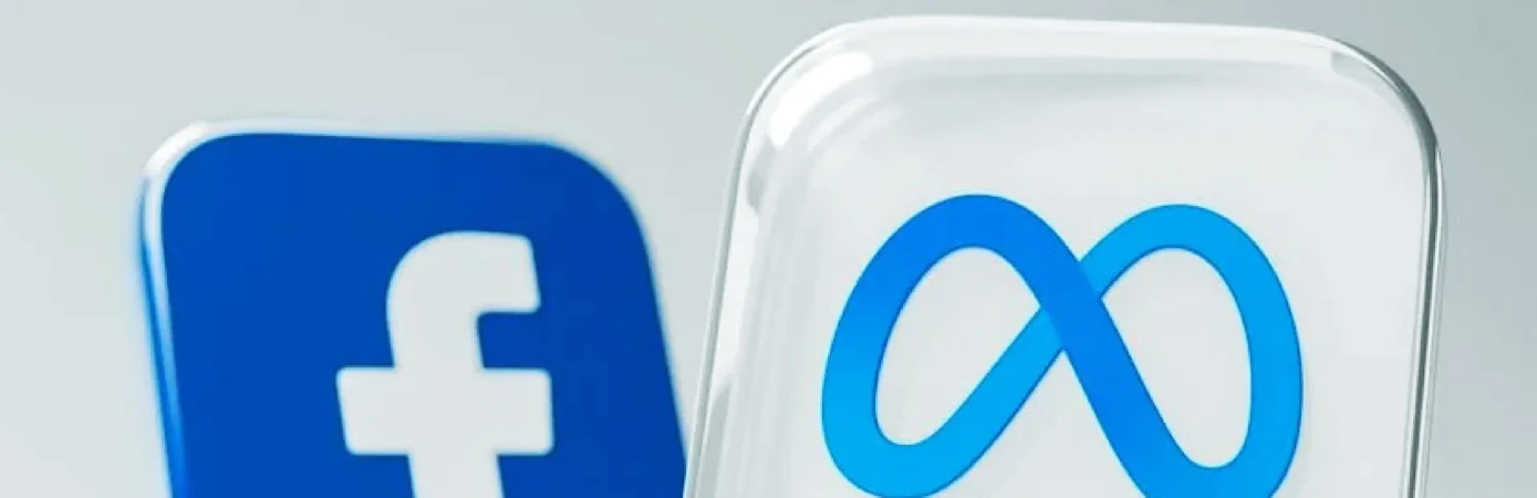 Close-up shot of the Facebook 'f' logo and Meta infinity loop logo, both in blue and encased in a clear, reflective material.