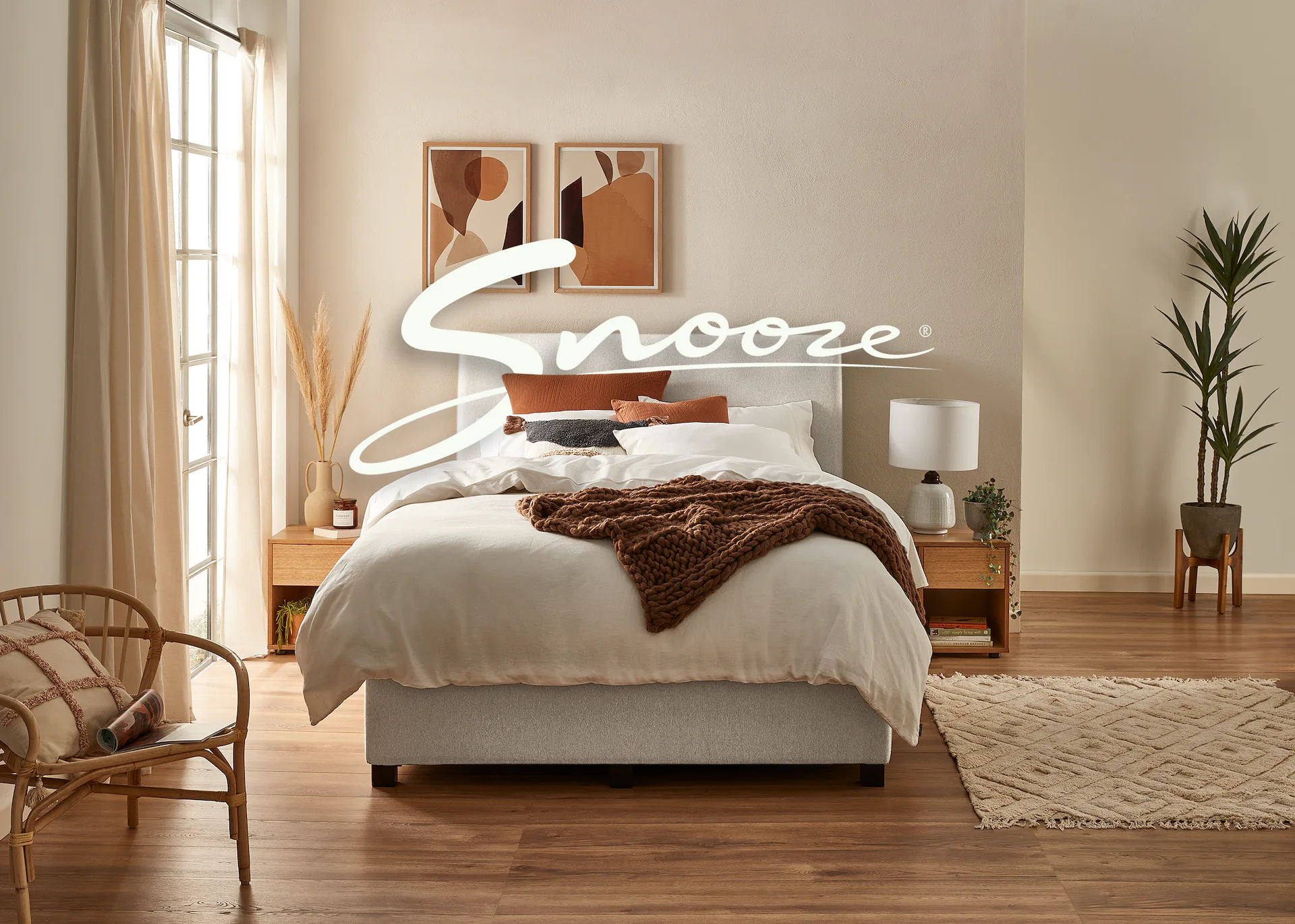 Bedroom interior showcasing a bed with white linens, a brown throw, and a rattan chair, complemented by warm wood tones and neutral decor.