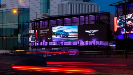 Large illuminated digital billboards displaying Genesis luxury vehicles mounted on a modern glass building exterior at night