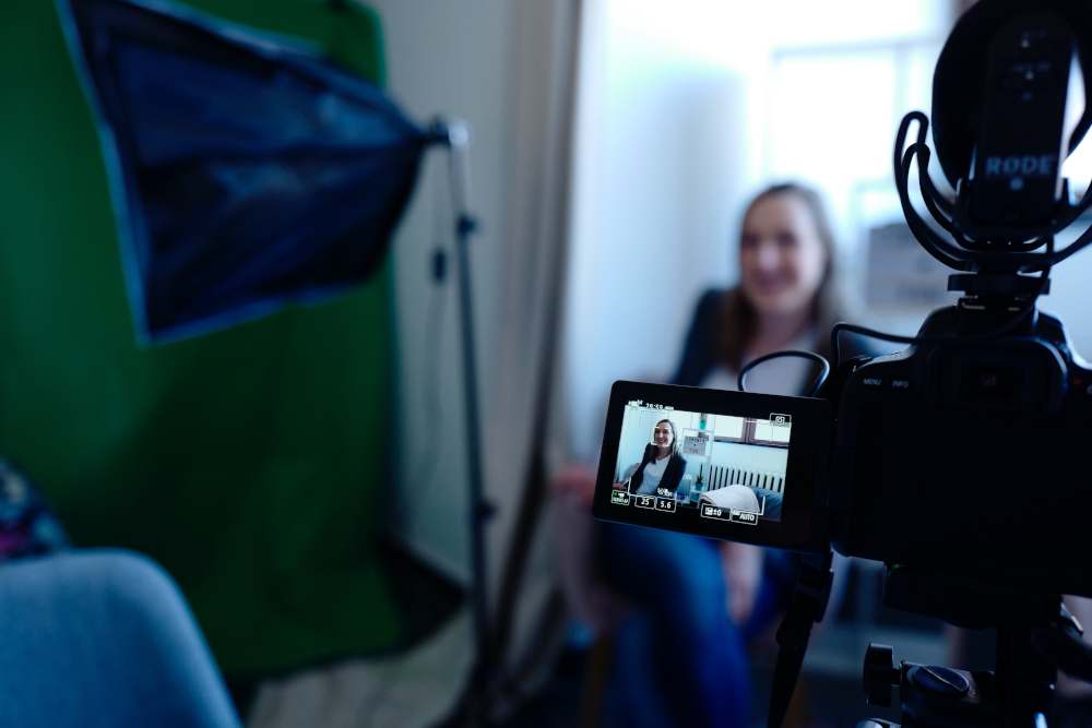 DSLR camera recording a woman with a softbox and green screen in the background, capturing video content with audio equipment.