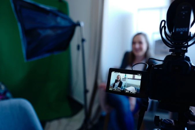 DSLR camera recording a woman with a softbox and green screen in the background, capturing video content with audio equipment.