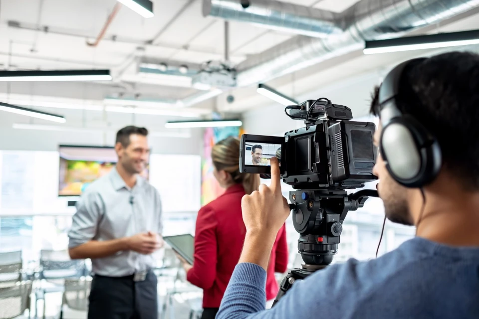 Filming an interview in a modern office space: a man is being interviewed while another person films with a professional video camera.
