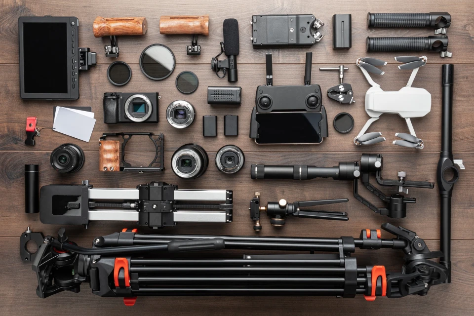 Overhead studio shot of diverse filmmaking equipment: camera, drone, microphone, tripod, lenses, monitor, and accessories on wood.