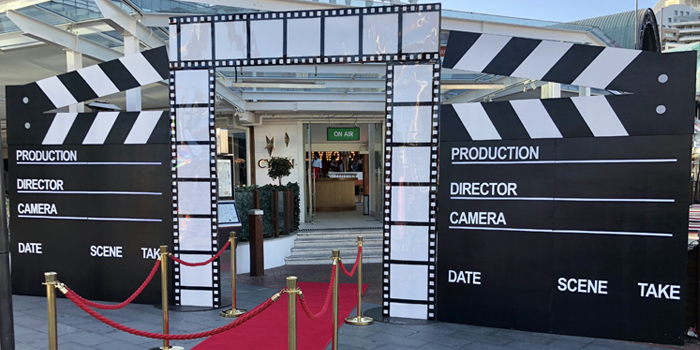 Red carpet entrance with two oversized film clapperboards and filmstrip columns at an event or party, indoor setting.